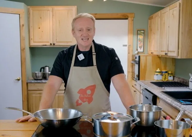 Fabrizio Tettamanzi in his kitchen, wearing an apron, with pots and pans on the stove